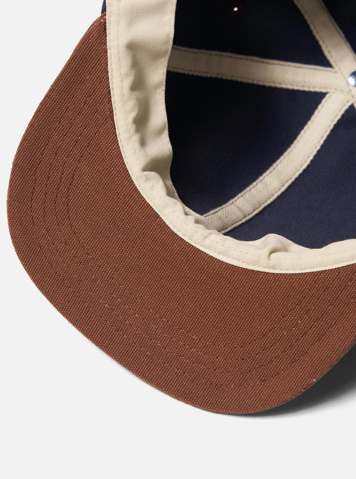 Close-up of the inside of a Navy/Brown Canvas Baseball Hat. The hat has a brown brim, navy canvas, and brown canvas lining. Shot on a white background.