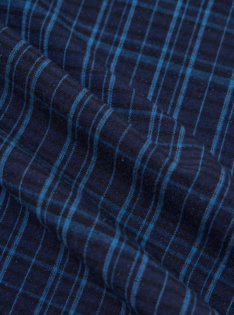 Close-up of the Indigo Plaid Long Pyjama Set fabric. The material is a soft, woven plaid in shades of indigo and light blue. The fabric is draped to show texture.