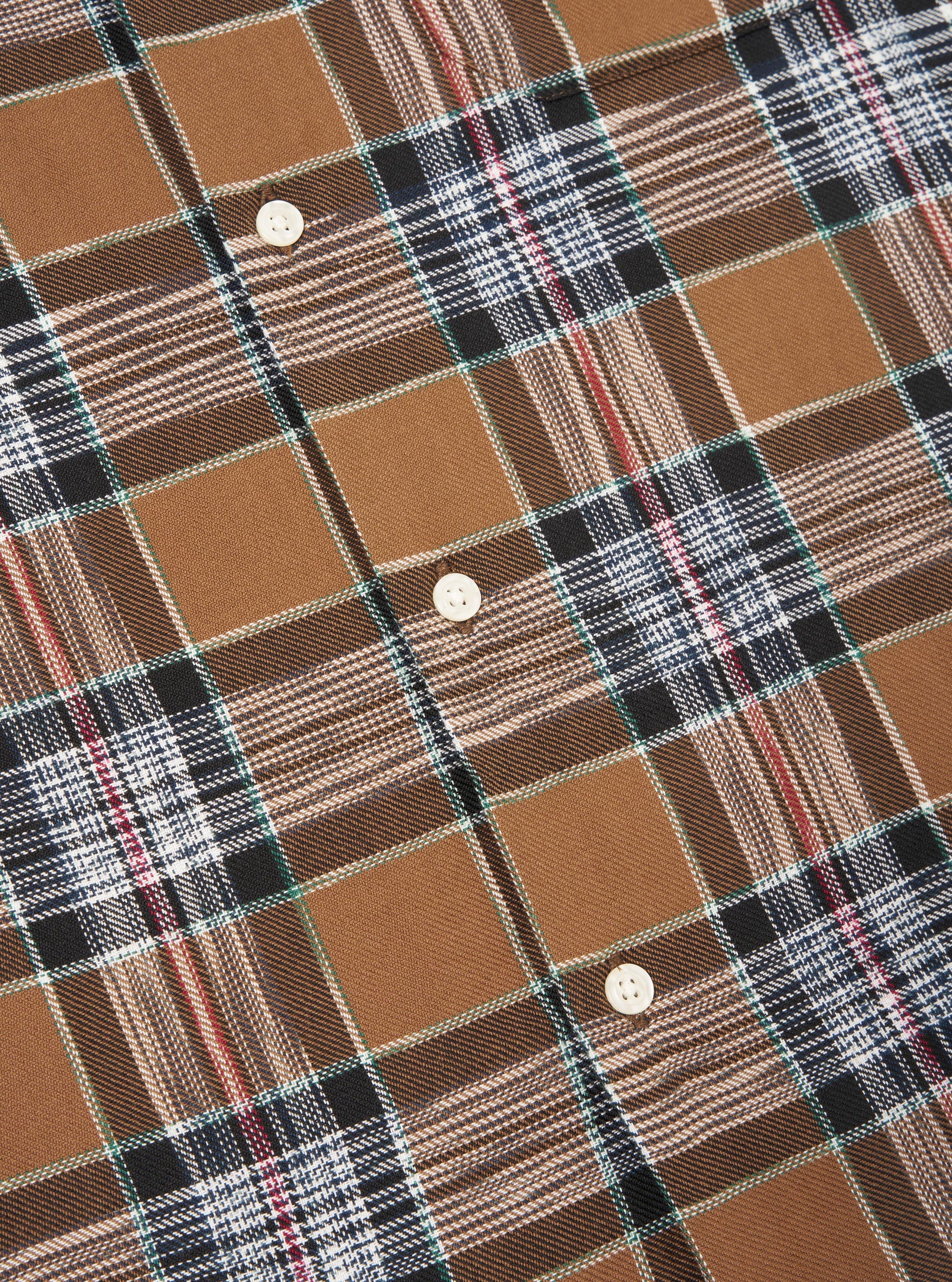 Close up of the brown ikat twill check long pyjama set. The fabric is a brown, black, white and red check with white buttons.
