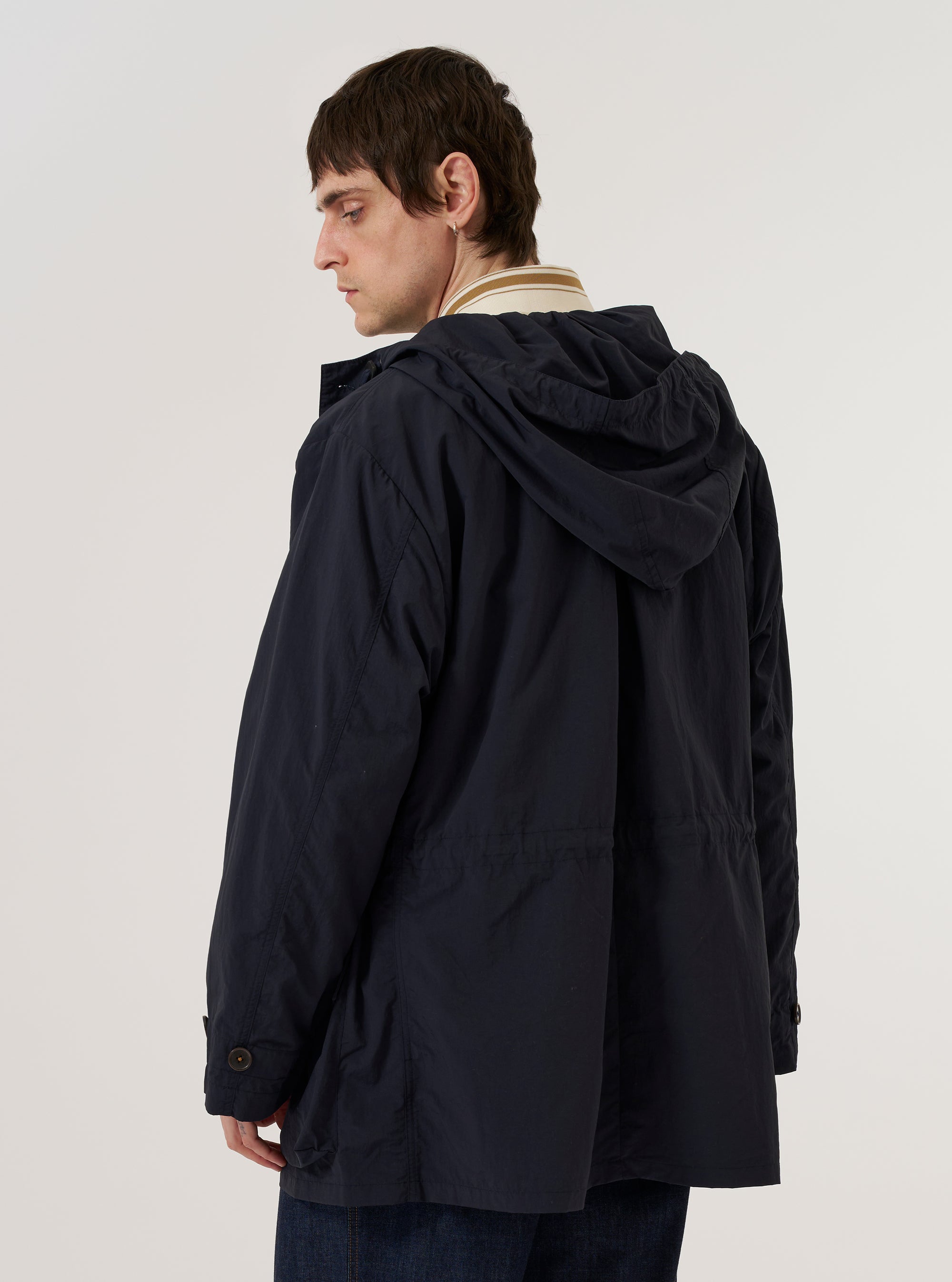 A model is wearing the Navy Seo Recycled Nylon Boston Parka, shown from a three-quarter rear angle against a plain white background. The parka features a longline silhouette, a large adjustable hood, and a clean back panel with a central vertical seam. The navy blue recycled nylon fabric has a smooth, technical appearance, and the model is wearing the hood up.