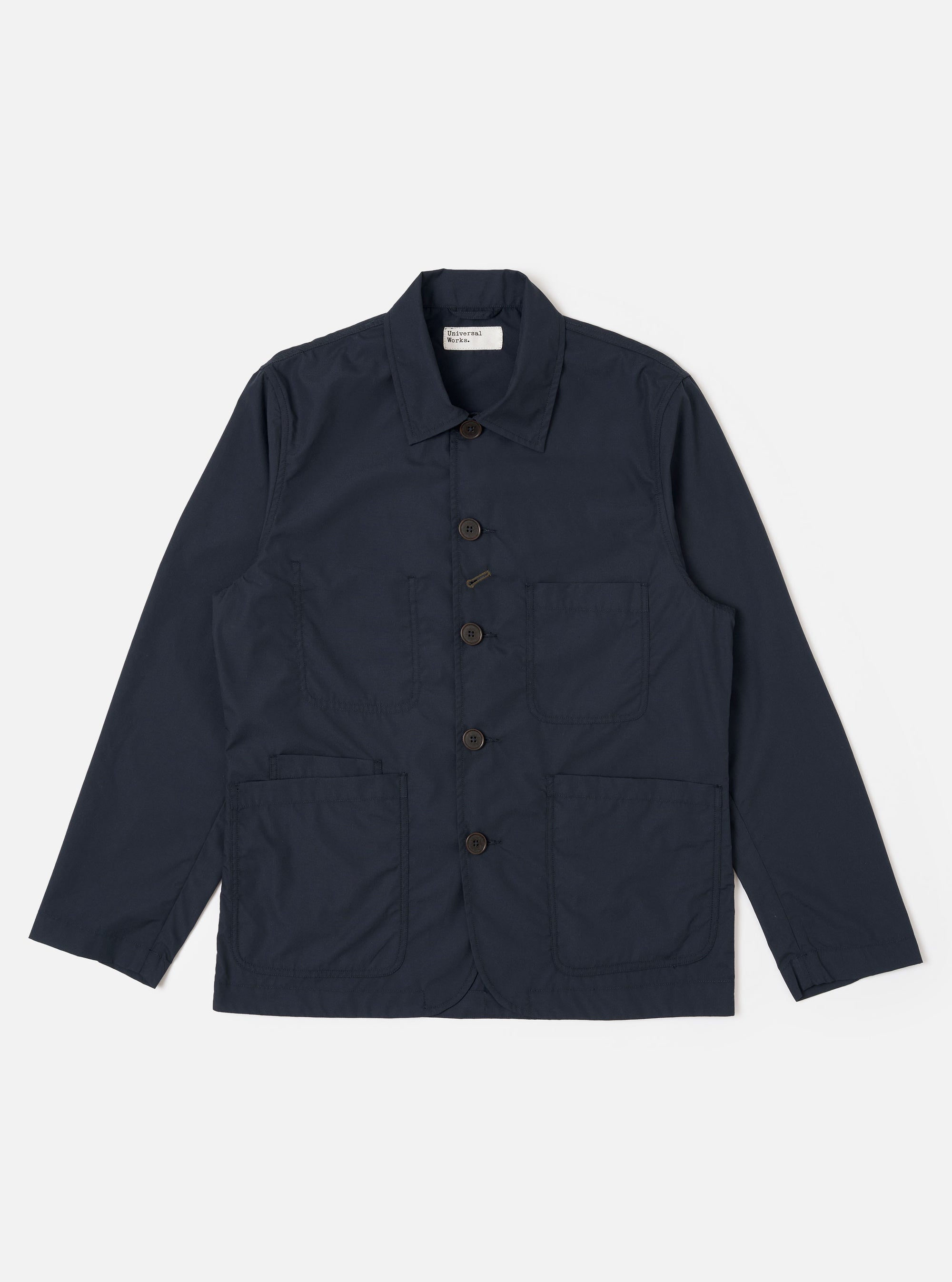 The Navy Recycled Polytech Bakers Jacket is displayed as a flat lay against a white background. The jacket features a five-button front closure with a signature angled buttonhole at the center, a classic collar, and four front patch pockets: one on the chest and three on the lower portion of the garment. The jacket is finished with a curved front hem and visible tonal stitching.