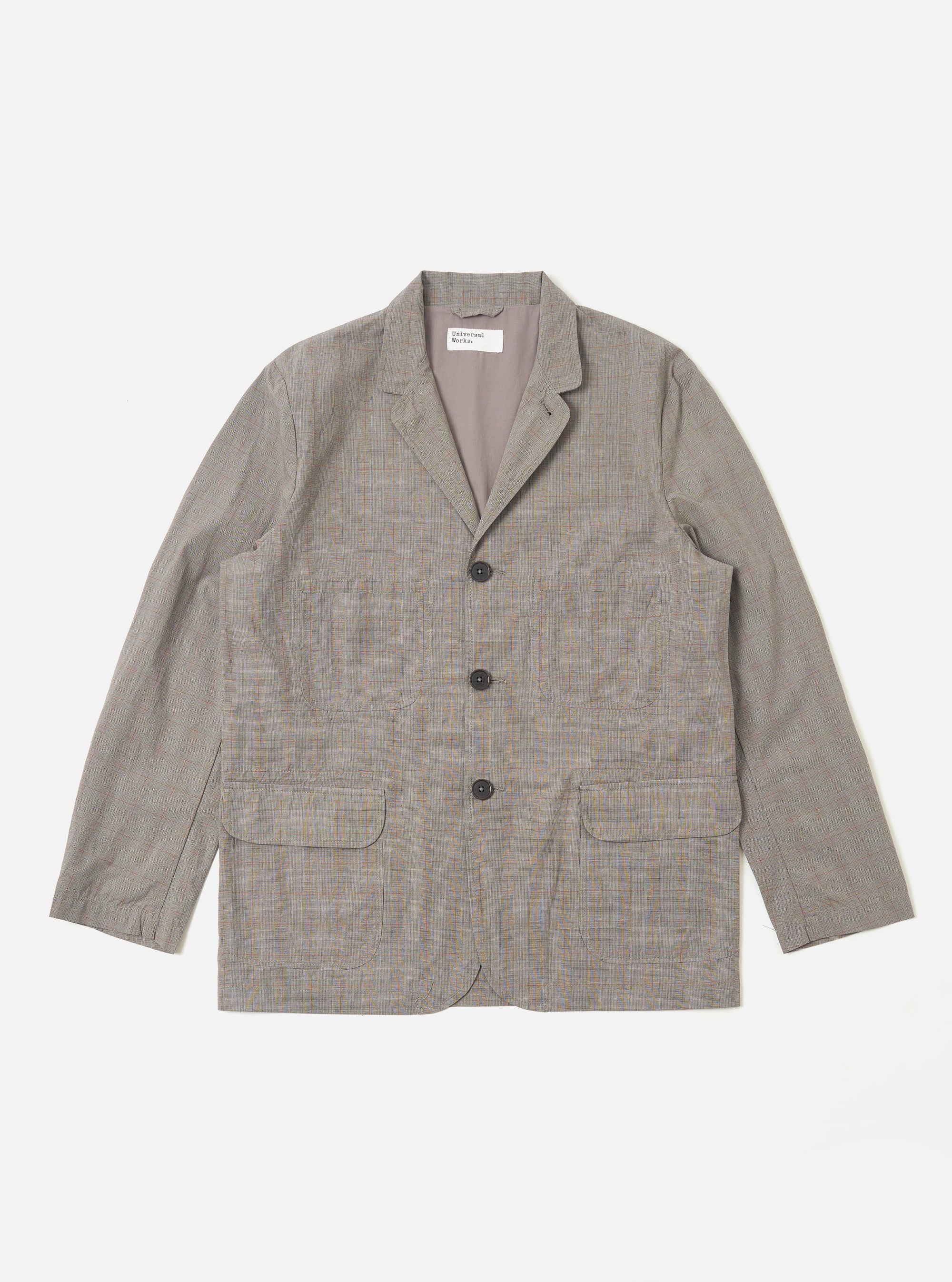 The Grey Brown Wales Glen Check Barra Jacket is shown as a flat lay against a white background. The jacket features a classic glen check pattern in shades of grey and brown, a three-button front closure, and two large patch pockets at the waist. The garment has a structured collar and a simple, clean design.