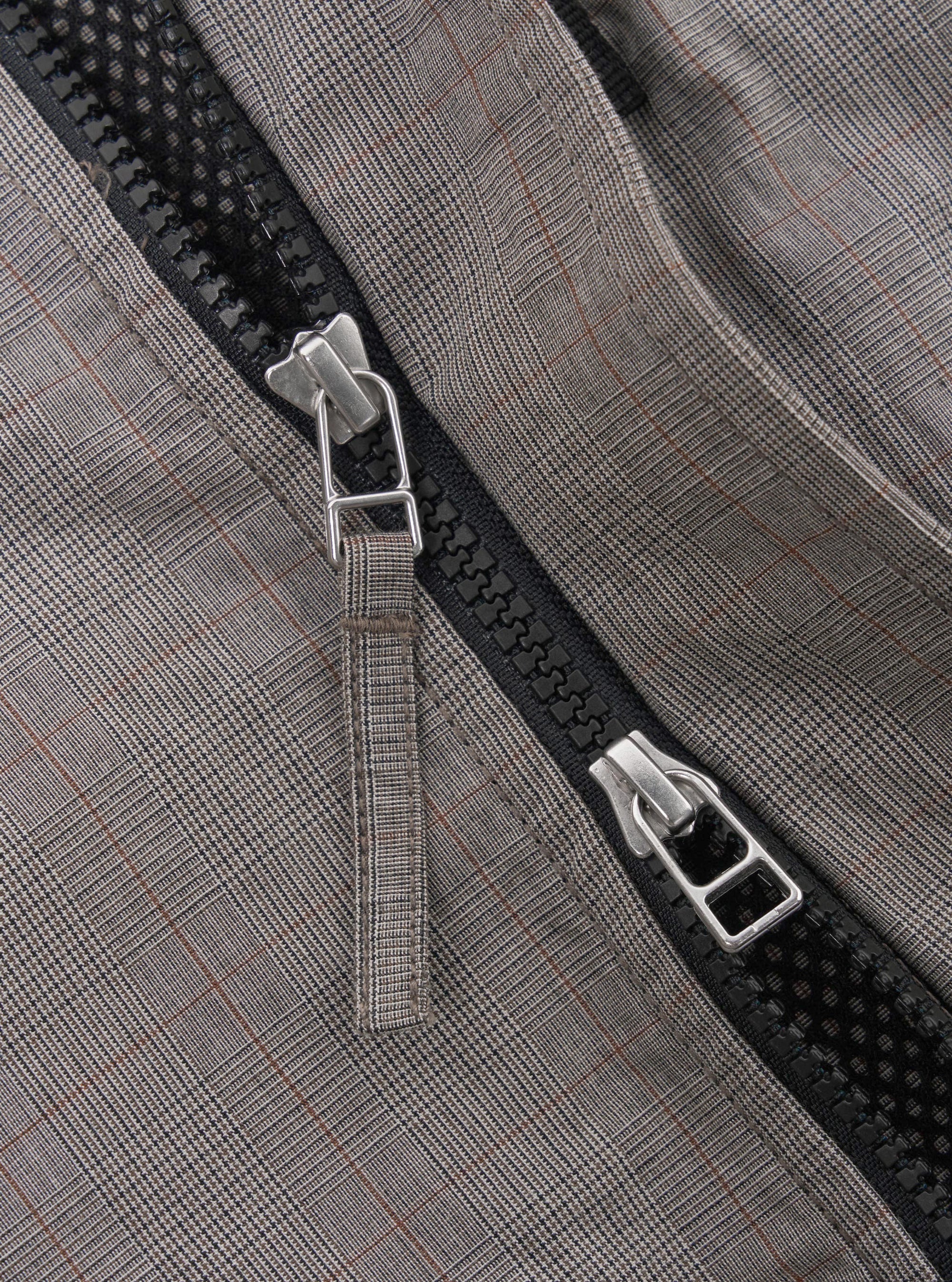 The Grey Brown Wales Glen Check NS Bomber Jacket is shown as a flat lay against a white background. The jacket features a regular fit with a partially concealed two-way zip front closure, metal pop studs, and large hand warmer pockets. The garment is made from a 100% cotton Glen check plaid fabric in grey and brown, accented by contrast stripe ribbing on the collar, cuffs, and hem.