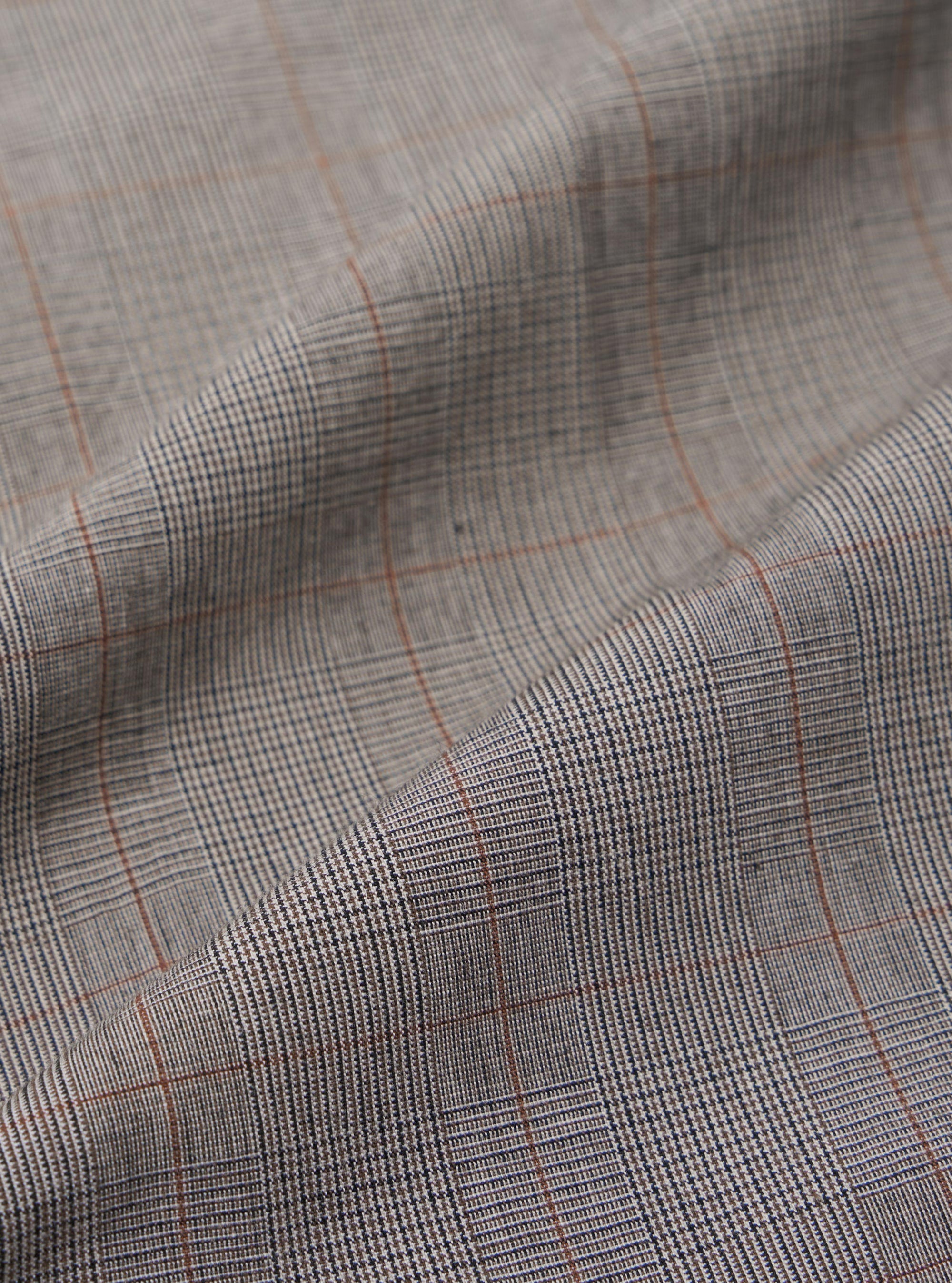 A close-up fabric swatch of the Grey Brown Wales Glen Check NS Bomber Jacket displays an intricate glen check pattern in shades of grey, light beige, and brown. The image highlights the detailed weave and color palette of the cotton fabric.