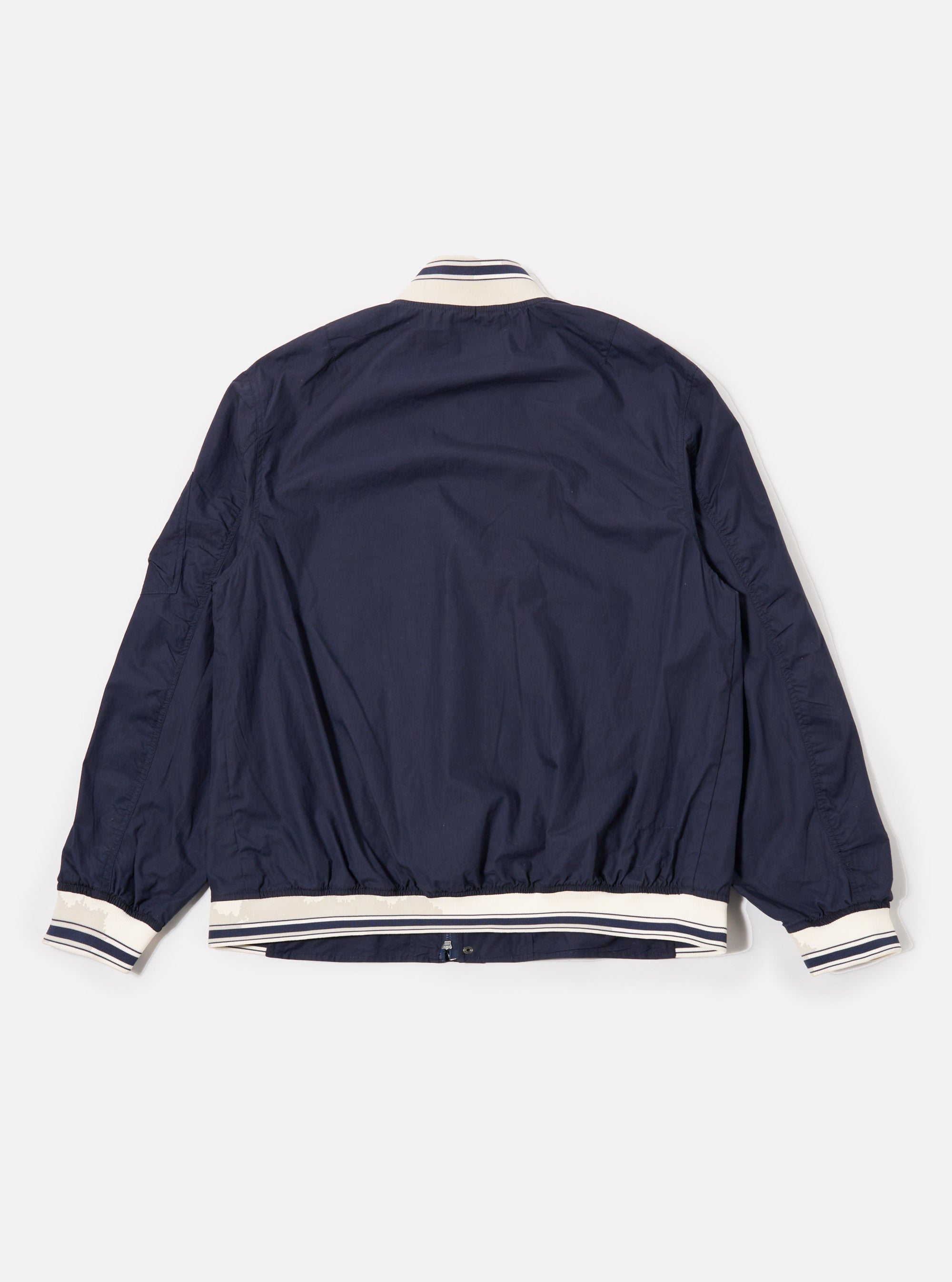 The Navy Peached Poplin NS Bomber Jacket is shown from the back as a flat lay against a plain white background. The image highlights the jacket's smooth navy blue fabric, a simple one-piece back panel, and tonal ribbed detailing at the collar, cuffs, and hem.