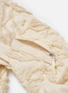 The Ecru 3D Flower NS Bomber Jacket is shown in a detail view as a flat lay against a plain white background. The image highlights the intricate 3D floral texture of the ecru-colored fabric and the construction of the large hand warmer pockets.