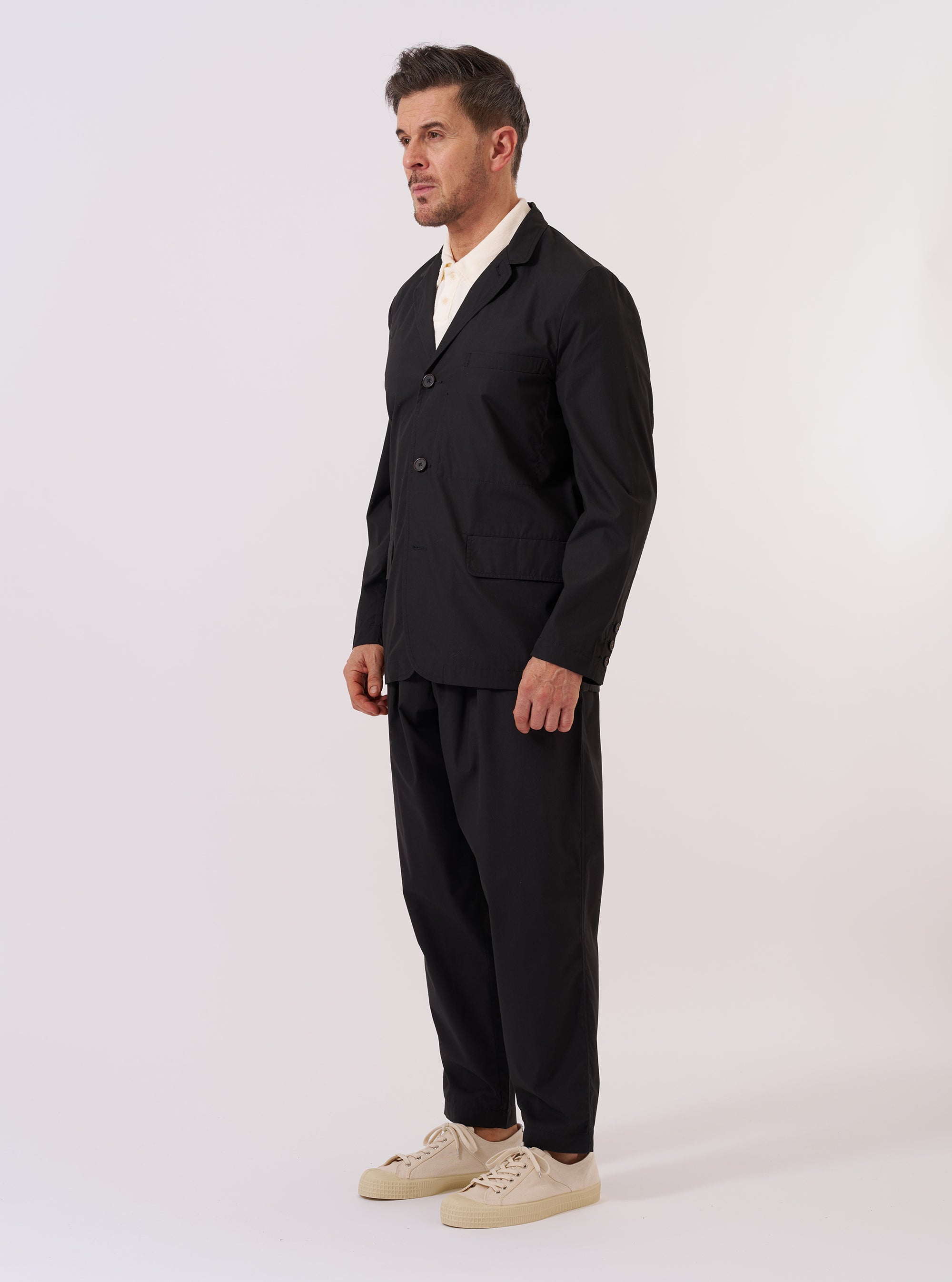 The Black Recycled Polytech Capitol Jacket is shown as a flat lay against a white background. The jacket features a notch lapel, a three-button front closure, and four front pockets with flap closures. The recycled polytech fabric has a smooth, matte finish.