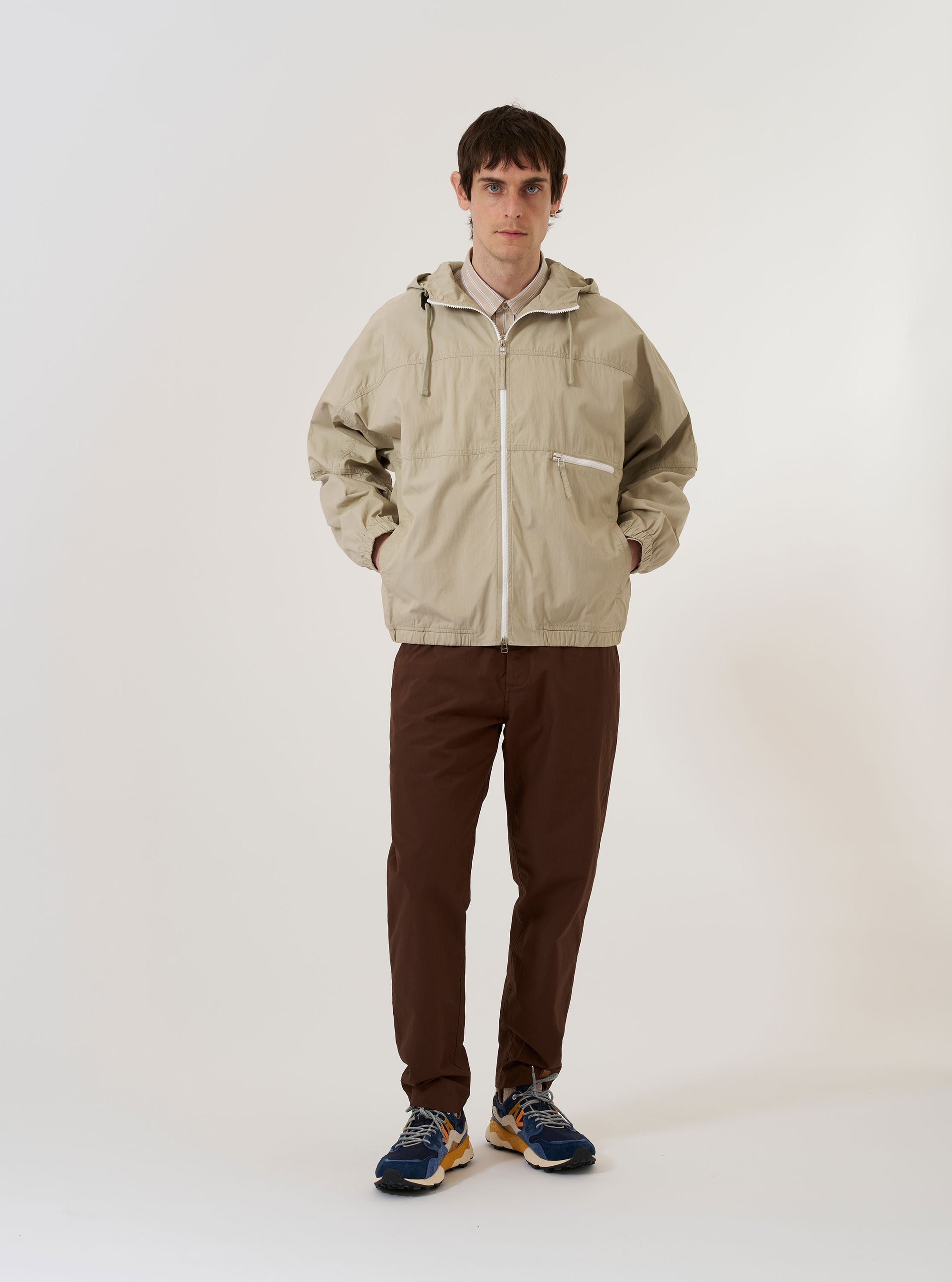 The Sand Cotton Recycled Nylon Mix Daley Jacket is shown as a flat lay against a plain white background. The jacket features a full-zip front, a spacious hood with a high neckline, and two large slanted patch pockets at the waist. The lightweight fabric is a solid sand color with a smooth, technical finish.