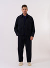 The Dark Navy Ospina Cotton Duty Jacket is shown as a flat lay against a white background. The jacket features two double-flap hip pockets, a single chest patch pocket, and a central button-down closure. The dark navy fabric has a visible seersucker texture, and the garment is designed with a curved hem and a structured collar.