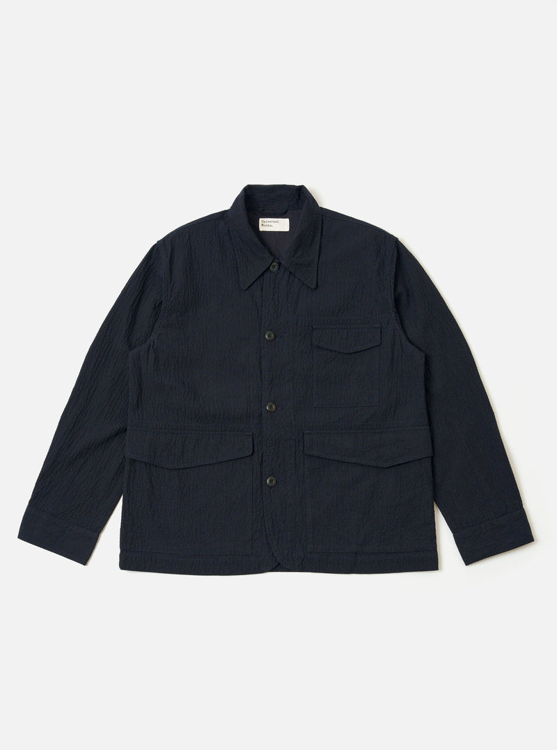 The Dark Navy Ospina Cotton Duty Jacket is presented as a flat lay against a plain white background. The jacket features a five-button front closure, a structured collar, and three prominent patch pockets on the front. The fabric displays a subtle, puckered seersucker texture.