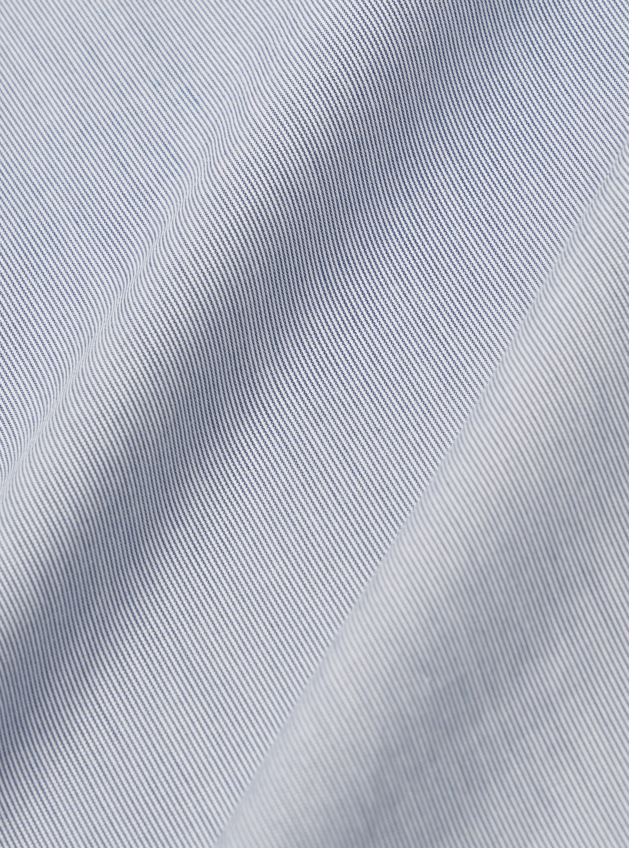 A close-up fabric swatch of the Navy Kennedy Stripe Labour Jacket displays the detailed pattern of the organic cotton material. The fabric features vertical white stripes of varying thicknesses set against a dark navy blue background.
