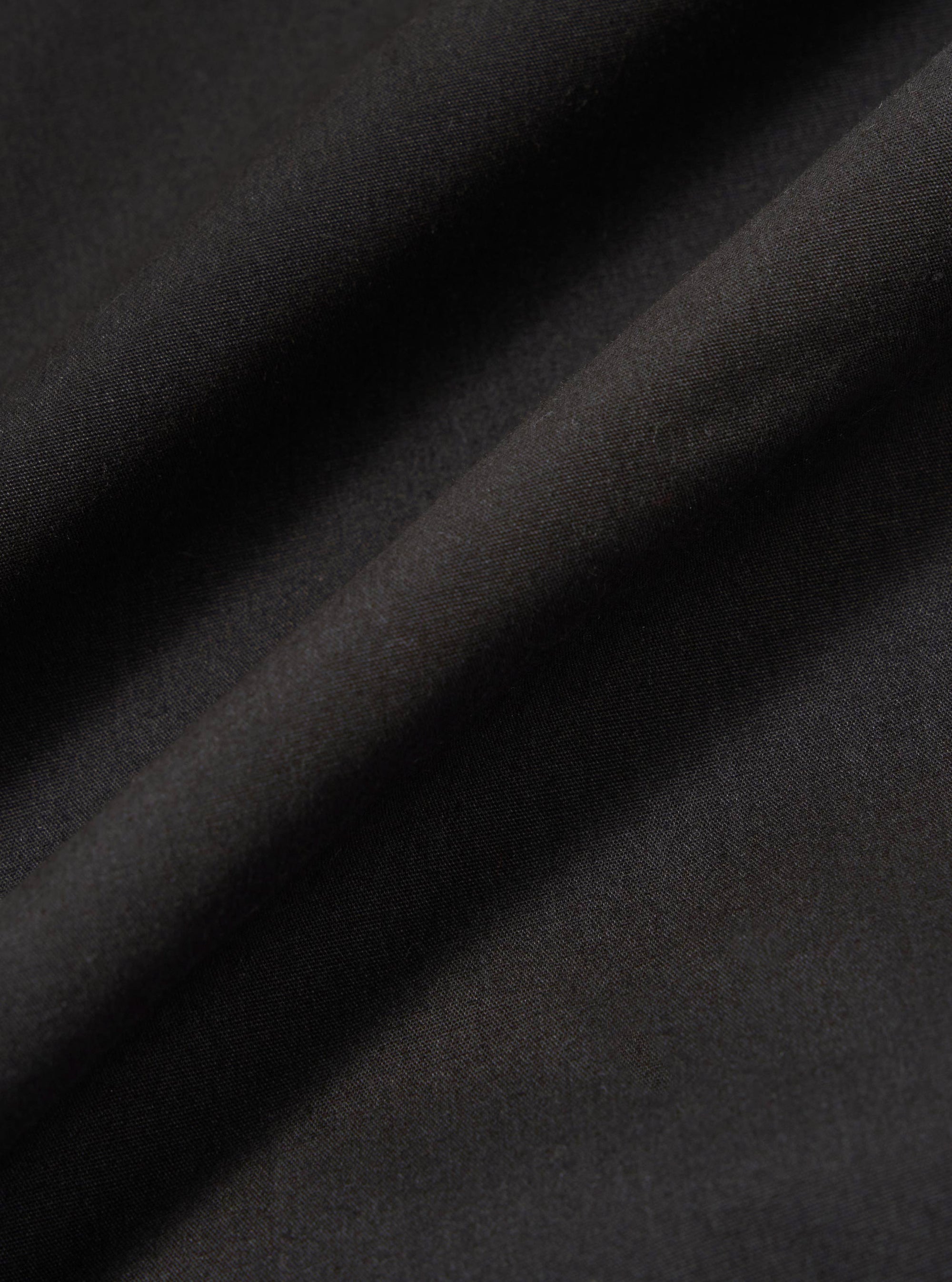 A close-up swatch image of the Black Recycled Polytech Rose Bowl Jacket highlights the smooth, technical texture of the black recycled polytech fabric. The material fills the frame, providing a detailed view of the garment's color and construction.