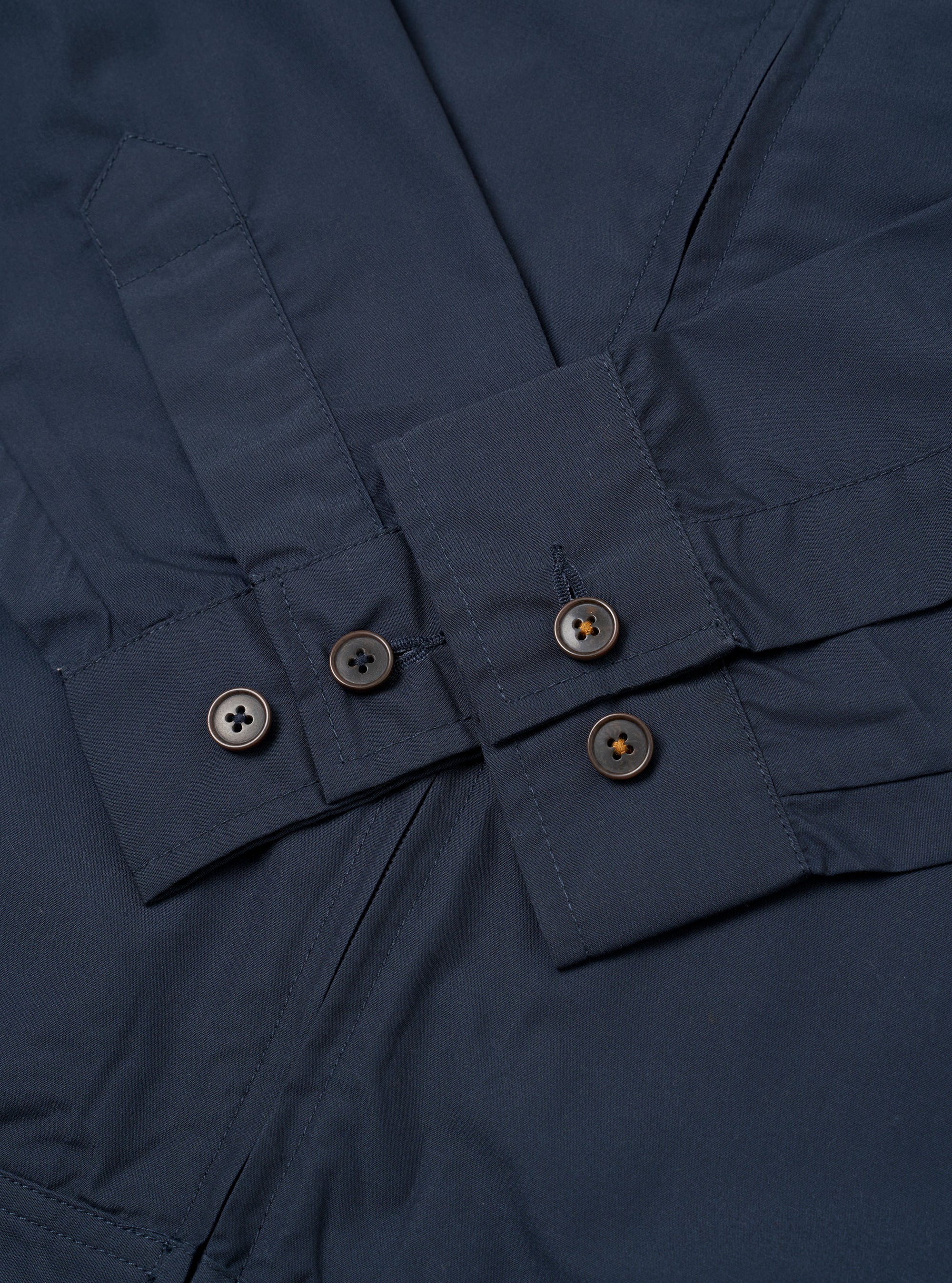 The Navy Recycled Polytech Rose Bowl Jacket is shown from the back as a flat lay against a plain white background. The image highlights the jacket's smooth navy blue fabric, a central vertical seam, and an adjustable back hem with a buttoned tab. The pleated details on the rear of the sleeves are also visible.