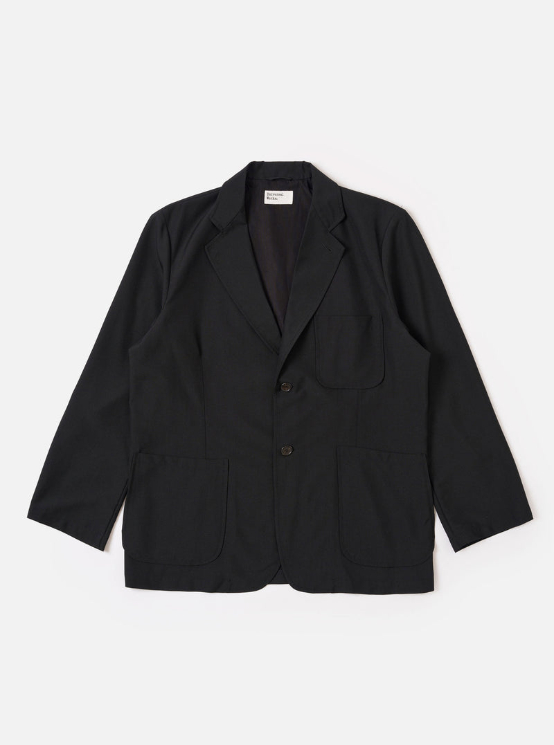 The Black Tropical Suiting Two Button Jacket is shown as a flat lay against a white background. The jacket features a relaxed fit with a long, wide notched lapel, two large lower patch pockets, and a single chest patch pocket. The two-button closure is visible at the center, and the fabric has a smooth, lightweight appearance.