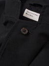 The Black Tropical Suiting Two Button Jacket is shown from the back as a flat lay against a plain white background. The image highlights the jacket’s clean tailoring, featuring a centered rear vent and visible vertical seams. The fabric has a smooth, lightweight appearance characteristic of tropical suiting.