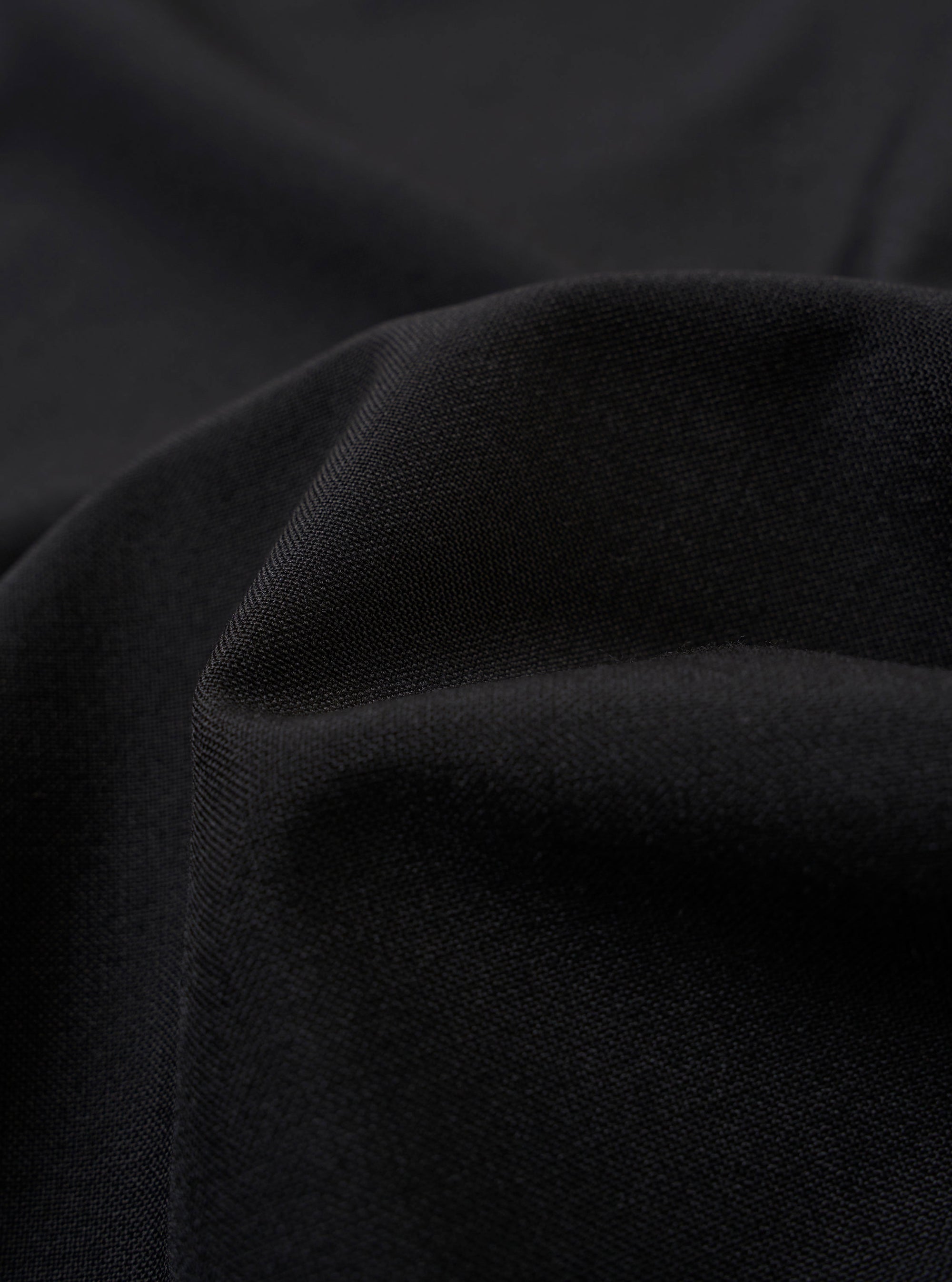 The Black Tropical Suiting Two Button Jacket is shown as a flat lay against a plain white background. The jacket features a classic two-button front closure, notched lapels, and two large patch pockets at the hip. The fabric appears smooth with a subtle sheen, characteristic of tropical suiting.