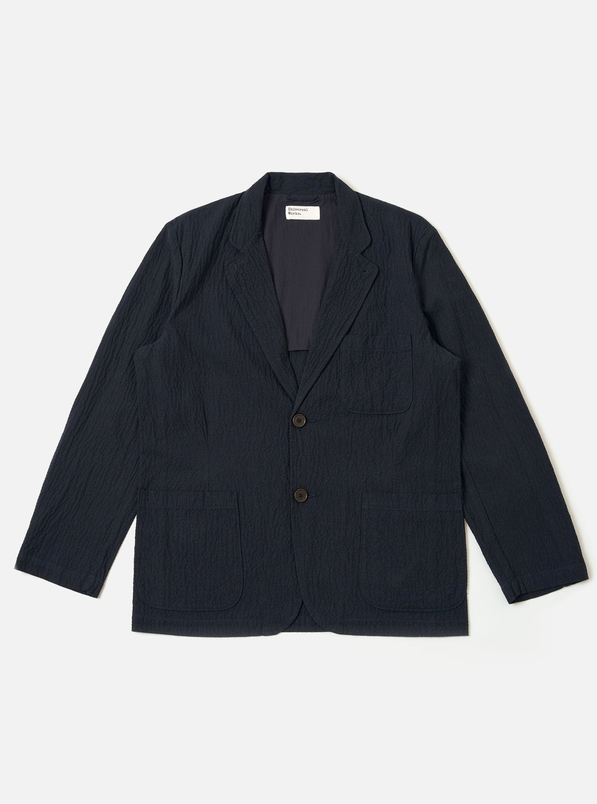 The Dark Navy Ospina Cotton Two Button Jacket is shown as a flat lay against a white background. The jacket features a two-button front closure, a long and wide lapel, two lower patch pockets, and a single chest patch pocket. The fabric has a visible puckered seersucker texture.
