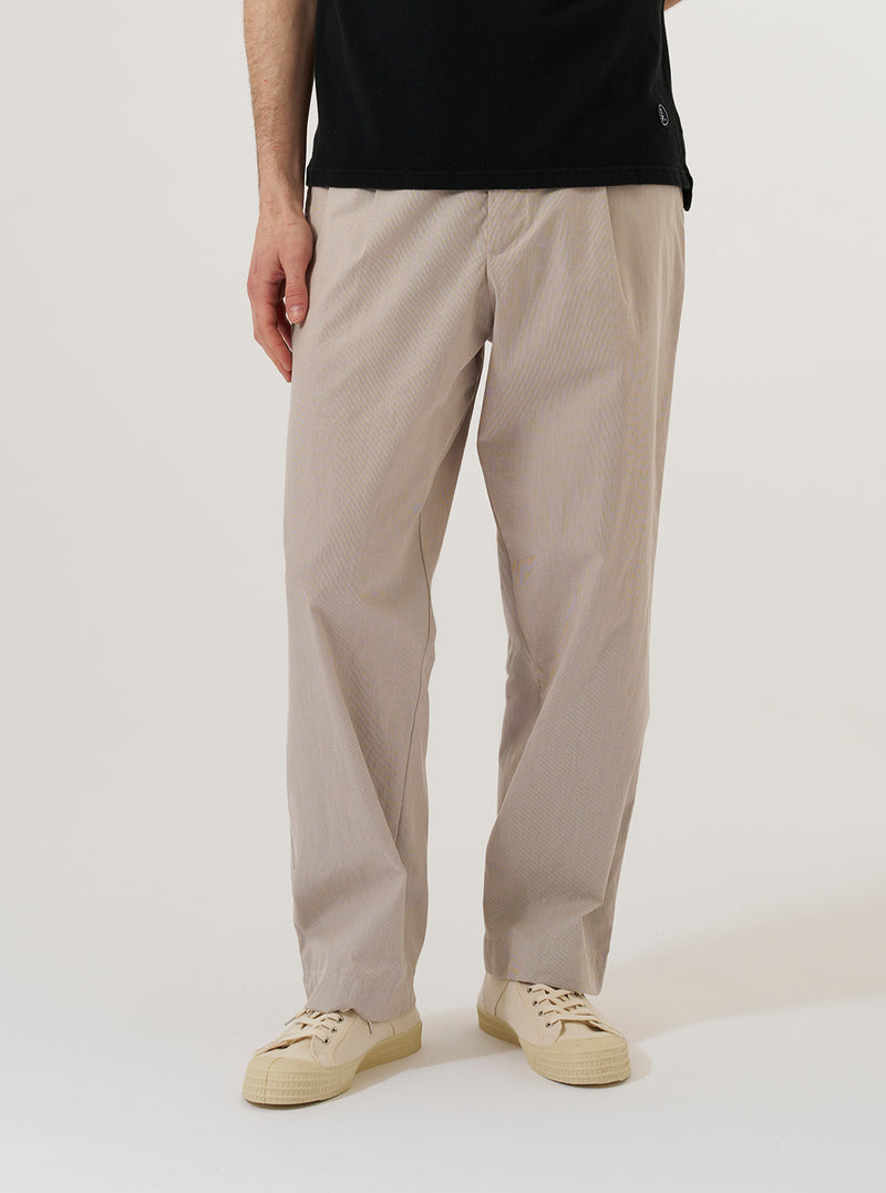 A model wears the Brown Kennedy Stripe Duke Pant, shown from the waist down against a plain white background. The trousers feature a loose, wide-leg fit with a brown and cream vertical stripe pattern throughout. They are styled with a tucked-in shirt and dark shoes, highlighting the pleated front and relaxed silhouette of the garment.