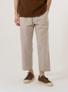 A model wears the Brown Kennedy Stripe Hi Water Trouser, shown from the waist down against a plain white background. The trousers feature a vertical pinstripe pattern, a relaxed fit with a tapered leg, and a slightly cropped length that hits above the ankle. They are designed with a drawstring waist and slanted side pockets.