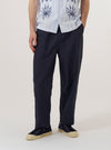 A model wears the Navy Peached Poplin Judo Pant, shown from the waist down against a plain white background. The image highlights the trousers' simple, straight-leg silhouette and relaxed fit. The model is wearing the navy blue cotton pants with the elasticated waistband visible, and the fabric has a soft, matte peached finish. One front pocket is visible on the side.