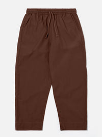The Brown Peached Poplin Judo Pant is shown as a flat lay against a white background. The trousers feature a relaxed, straight-leg silhouette with an elasticated waistband and an integrated drawstring. Two front pockets and a subtle hanging loop on the waistband are visible. The brown cotton fabric has a soft, matte finish characteristic of peached poplin.