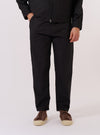 A model wears the Black Recycled Polytech Military Chino, shown from the waist down against a plain white background. The image highlights the slim-straight fit of the trousers, which feature a button fly, belt loops, and front pockets. The model is wearing the black chinos with a white t-shirt tucked in and white socks.