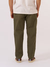 A model wears the Olive Recycled Polytech Military Chino, shown from the waist down against a plain, neutral studio background. The image highlights the wide but tapered fit of the trousers, which are made from a smooth olive green recycled polyester and cotton blend. The model is captured from a side angle, showcasing the tailored silhouette and the clean finish of the technical fabric. No mannequin is present in the image.
