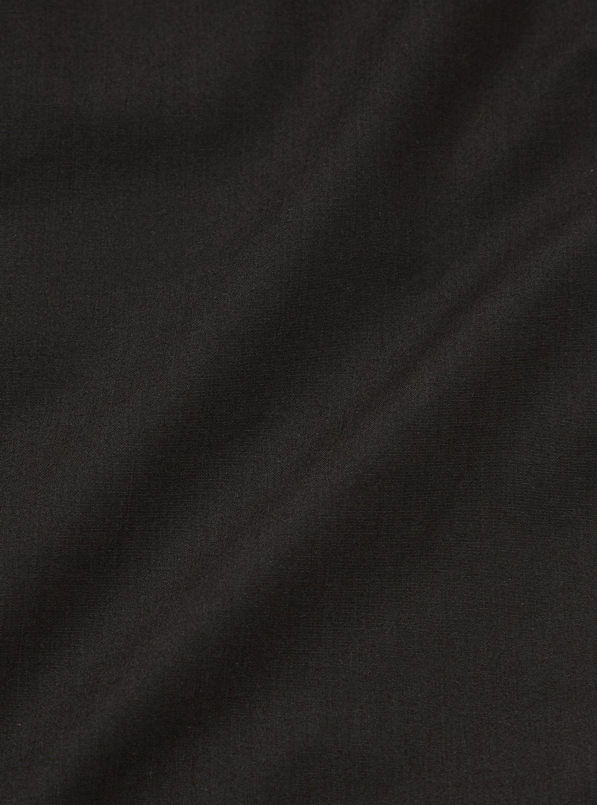A close-up swatch image of the Black Recycled Polytech Military Chino fabric. The image focuses on the deep black color and the smooth, technical texture of the recycled polyester and cotton blend.
