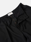 The Black Tropical Suiting Pleated Track Pant is shown from the back as a flat lay against a plain white background. The image highlights the two rear pockets, including one with a button-down flap, and the elasticated waistband. The lightweight black tropical suiting fabric, made of a polyester and wool blend, appears smooth and crisp.