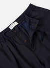 The Navy Tropical Suiting Pleated Track Pant is shown from the back as a flat lay against a plain white background. The image highlights the two rear set-in pockets, one with a buttoned flap and one button-jetted, as well as the elasticated waistband. The fabric is a smooth, dark navy tropical suiting with a visible fine-weave texture.
