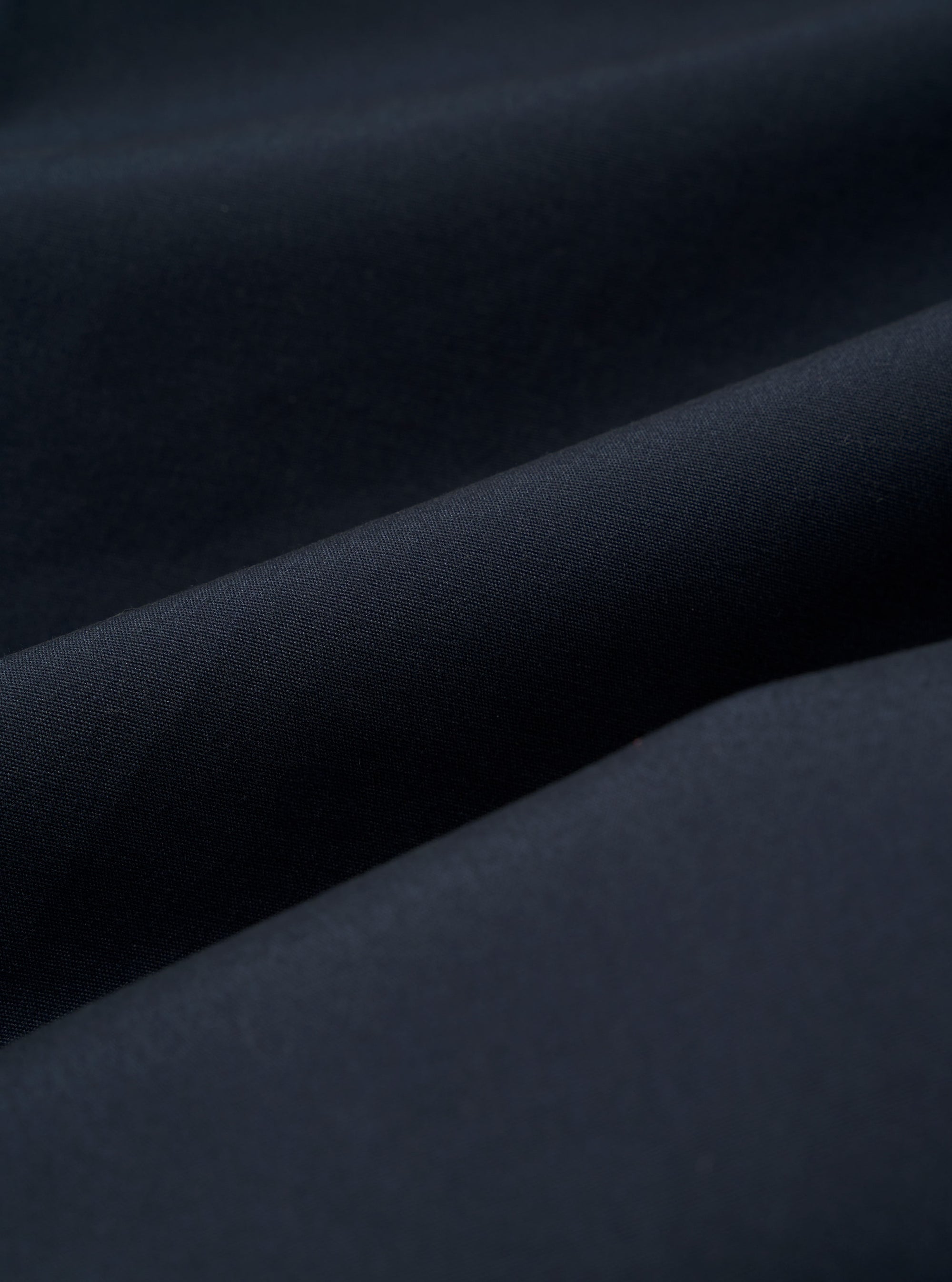 The Navy Recycled Polytech Pleated Track Pant is shown from a rear angle as a flat lay against a plain white background. The image highlights the elasticated waistband and two rear pockets, including one with a buttoned flap and one jetted pocket. The dark navy fabric appears smooth with a technical finish.