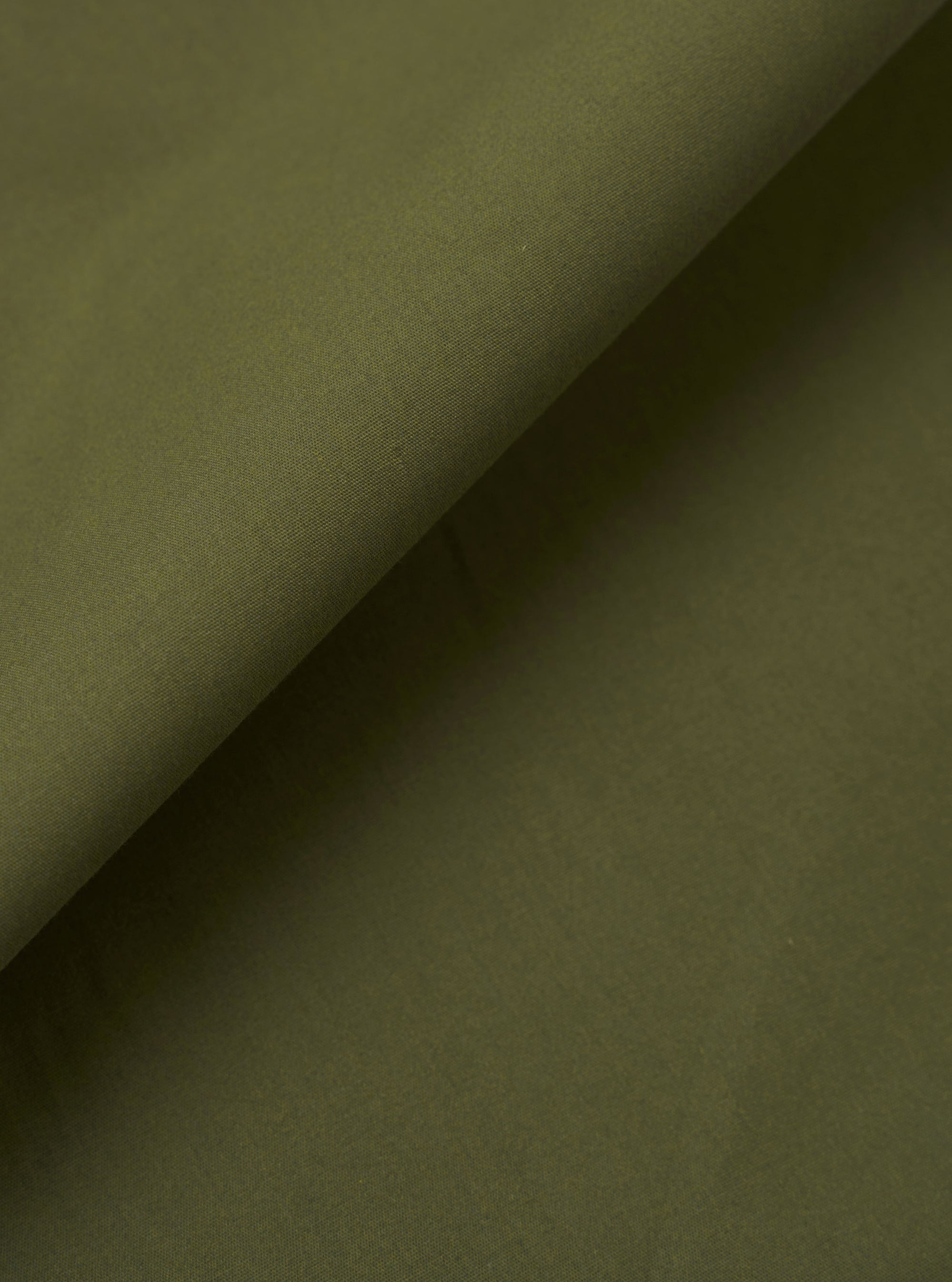 A close-up fabric swatch of the Olive Recycled Polytech Pleated Track Pant highlights the smooth, compact weave of the olive green material. The technical fabric, a blend of recycled polyester and cotton, is shown in detail to emphasize its uniform color and clean, utilitarian texture.