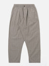 The Grey Brown Wales Glen Check Pleated Track Pant is shown as a flat lay against a plain white background. The trousers feature a single front pleat, an elasticated waistband with a matching drawstring, and two side slant pockets. The cotton fabric showcases a detailed grey and brown glen check pattern throughout the loose, tapered silhouette.