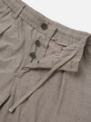 The Grey Brown Wales Glen Check Pleated Track Pant is shown as a flat lay against a white background. The trousers feature a grey and brown Glen check pattern, an elasticated waistband with a drawstring, and a single front pleat on each leg. The image highlights the loose, tapered fit and the texture of the cotton fabric.