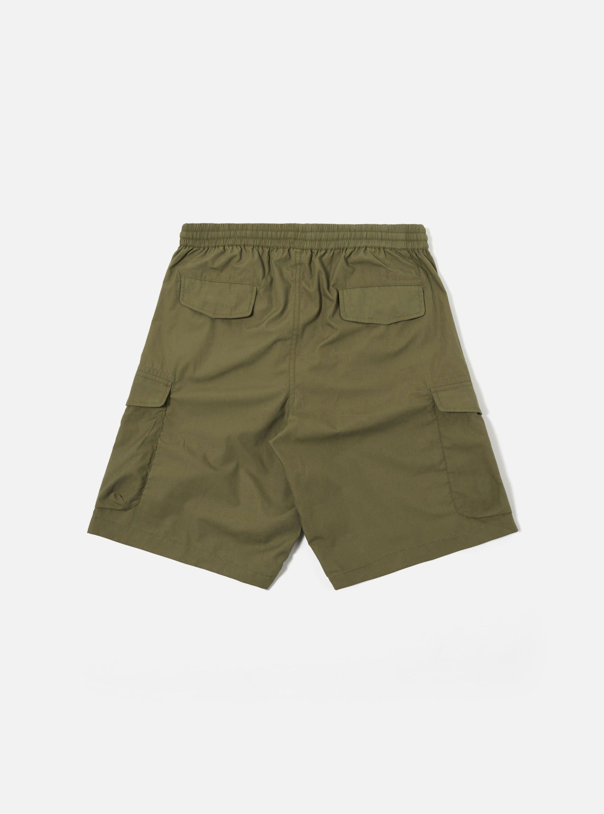The Olive Recycled Polytech Parachute Short is shown from the rear as a flat lay against a plain white background. The image highlights the back of the shorts, featuring two button-flap accordion patch pockets and an elasticated waistband. The fabric is a solid olive green with a smooth, technical finish.