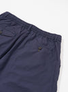 The Navy Peached Poplin Pleated Track Short is shown from a rear angle as a flat lay against a plain white background. The image highlights the elasticated waistband and two rear button-close pockets, one of which is a jetted pocket. The dark navy cotton poplin fabric has a smooth, matte finish.