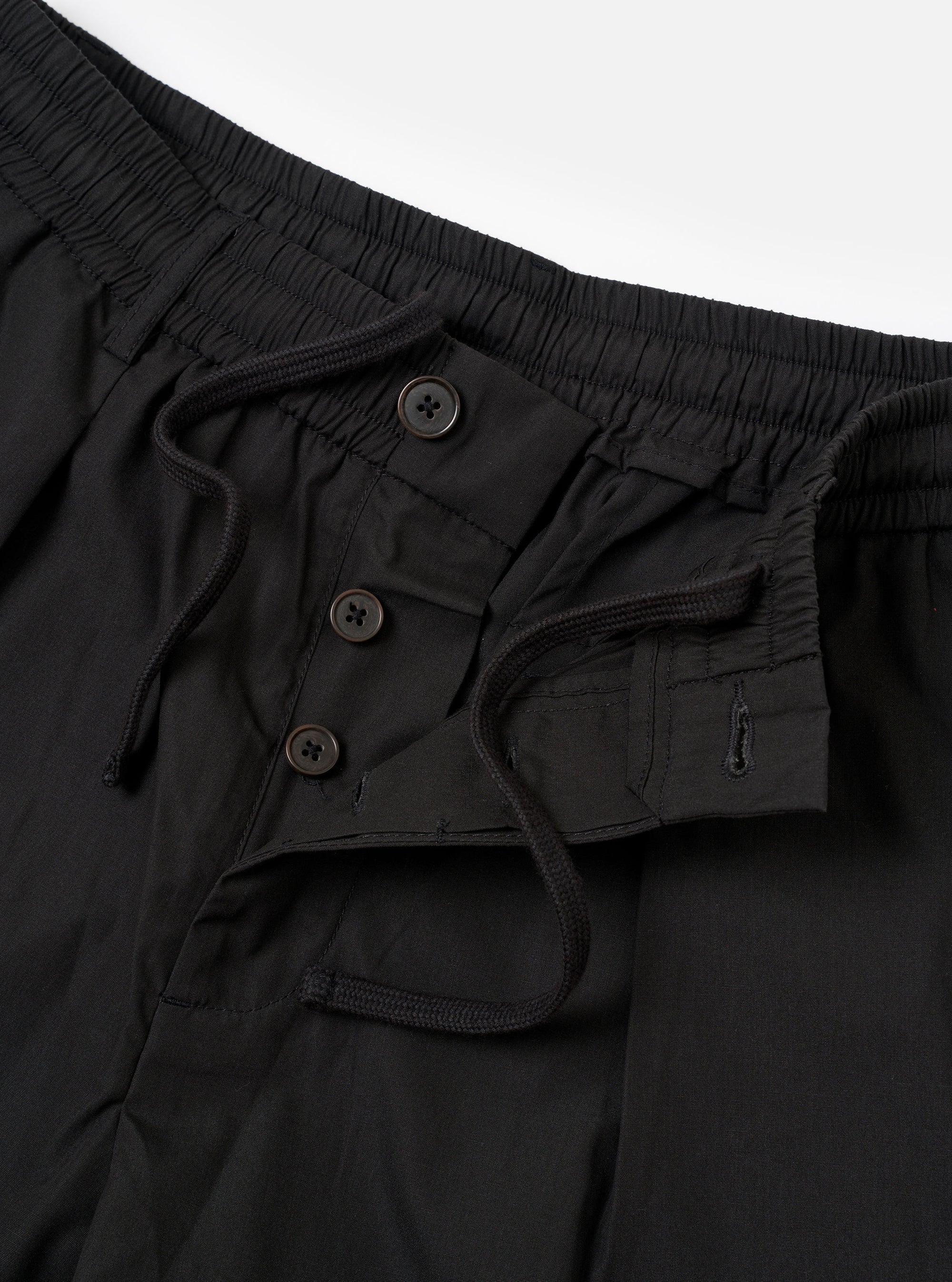 The Black Recycled Polytech Pleated Track Short is shown from the back as a flat lay against a plain white background. The shorts feature an elasticated waistband and a single rear patch pocket on the right side. The black fabric has a smooth, technical appearance with visible tonal stitching.