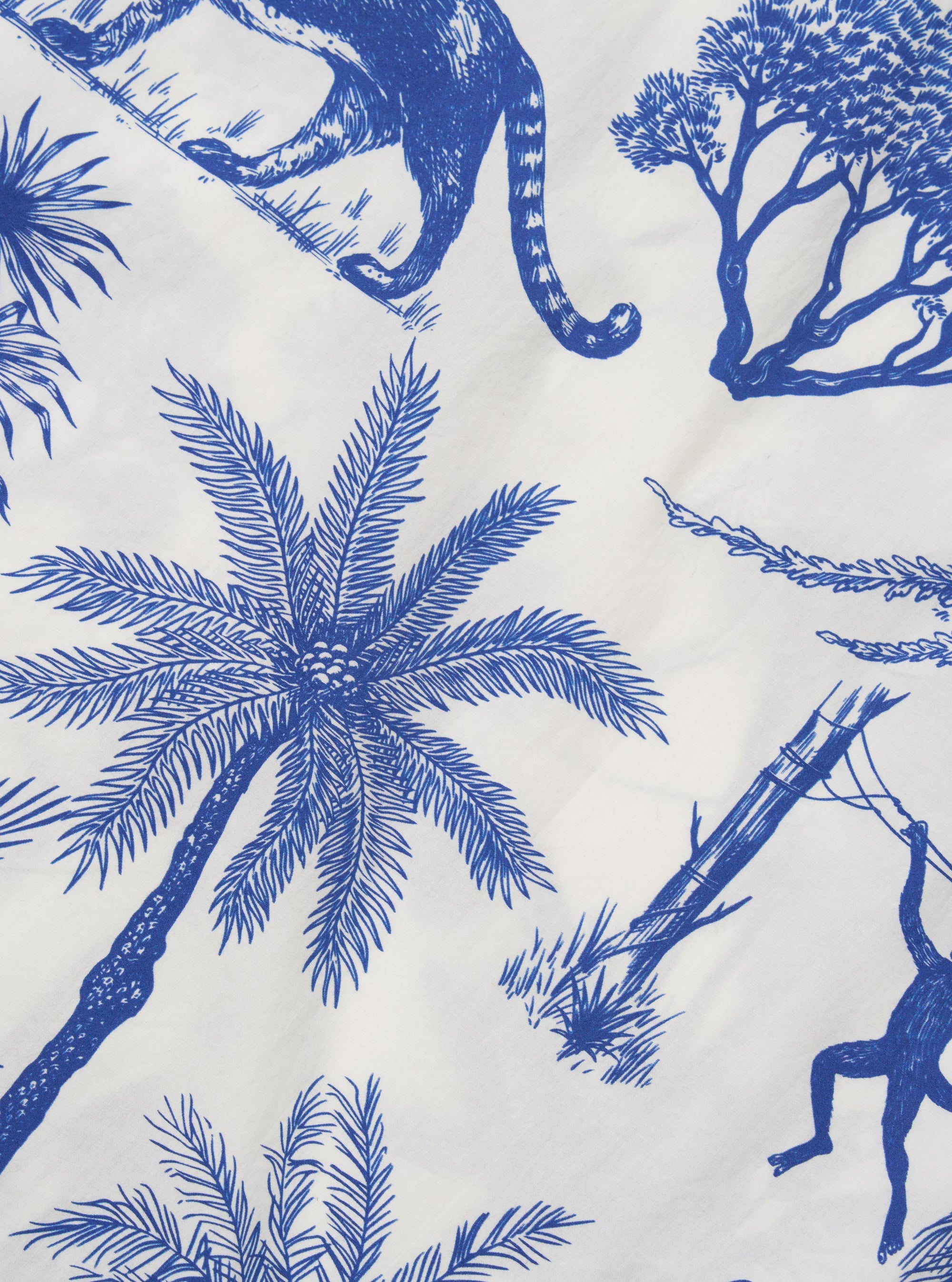 A close-up fabric swatch of the White Jungle Toile Poplin Fatigue Shirt highlights the intricate jungle toile print on white cotton poplin. The design features various animals and tropical foliage illustrations in a dark shade.
