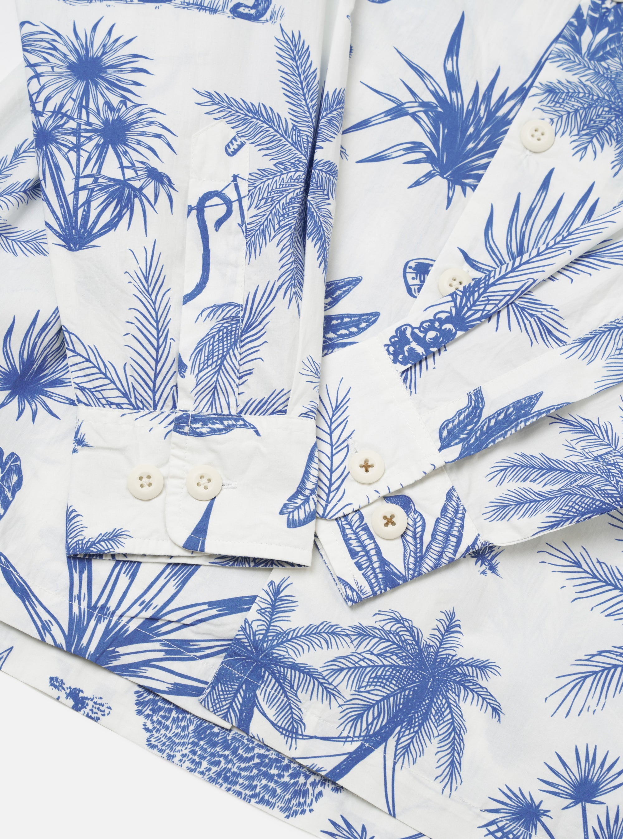 The White Jungle Toile Poplin Fatigue Shirt is shown in a detail view as a flat lay against a plain white background. The image focuses on the lower portion of the garment, highlighting the intricate dark botanical print on the white cotton poplin fabric and the clean stitching of the straight hem and side seam.