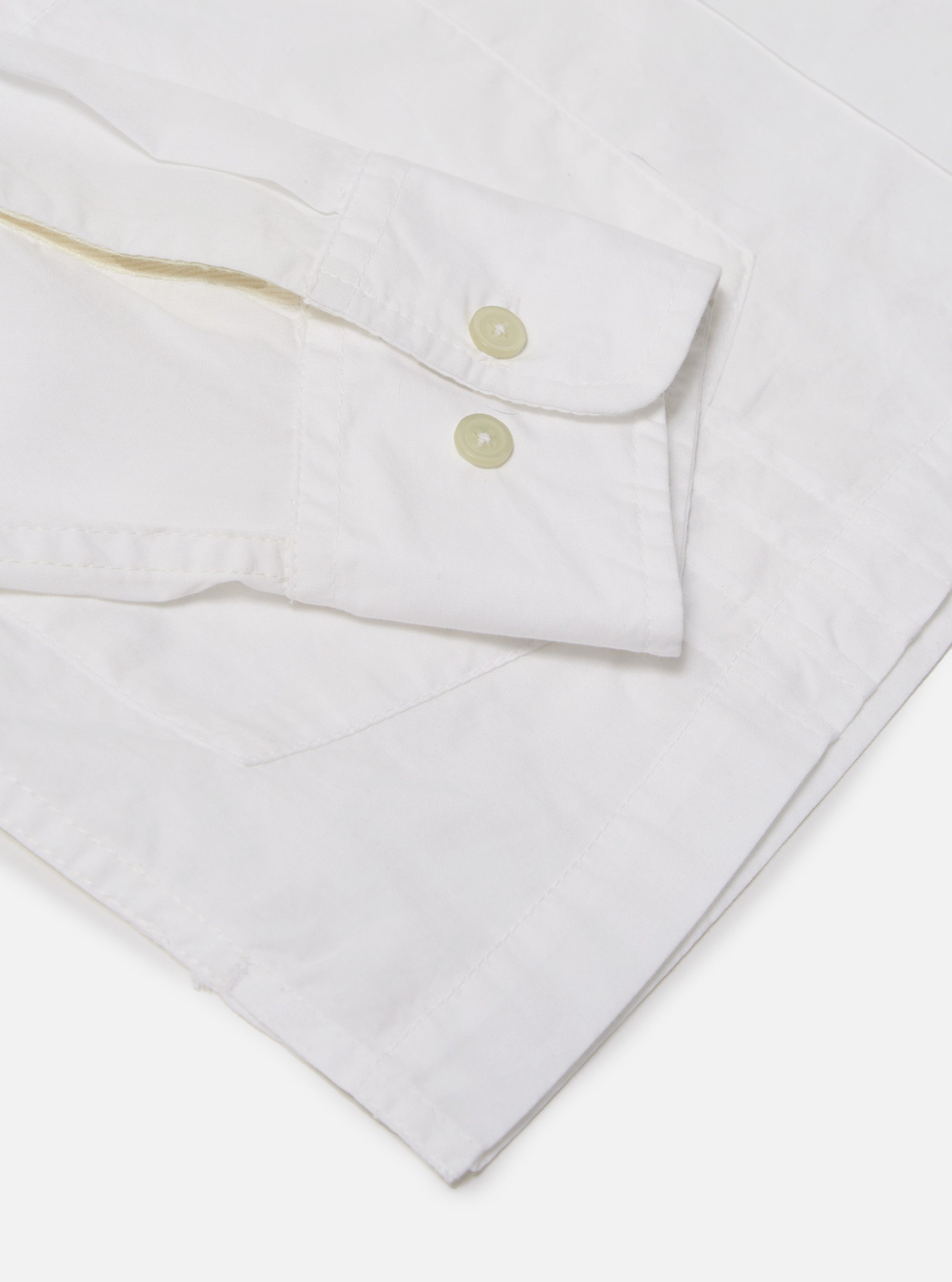 The White Poplin Dwight Overshirt is shown in a detail view as a flat lay against a white background. This view focuses on the lower portion of the garment, showcasing the straight hem and two of the four front patch pockets. The crisp white cotton poplin fabric features a smooth texture.