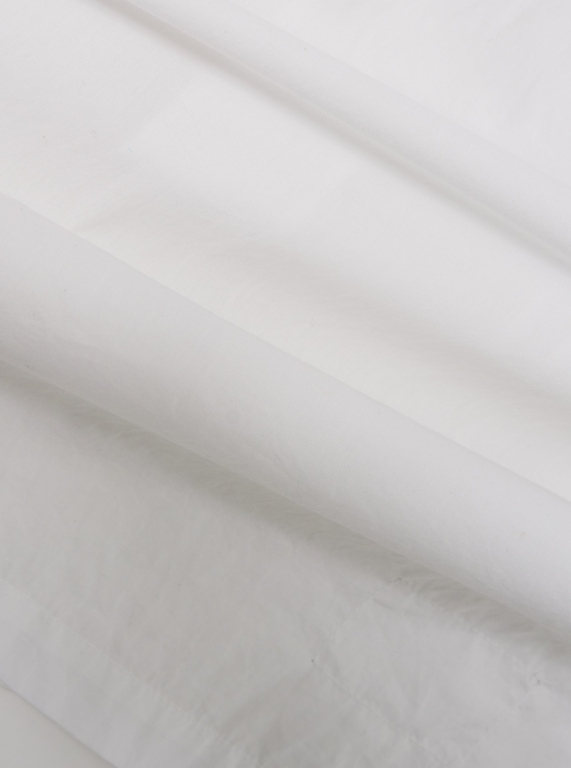 A close-up swatch of the White Poplin Dwight Overshirt highlights the smooth and tightly woven texture of the white cotton poplin fabric. The material fills the frame, providing a detailed view of the garment's clean, crisp finish and solid white color.