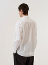 A model wears the White Poplin Patched Lazy Day Shirt against a plain white background. The shirt features a relaxed fit, a button-down front with tonal buttons, and prominent rectangular fabric patches on the chest. The model is shown from the waist up, wearing the crisp white poplin garment tucked into olive green trousers.