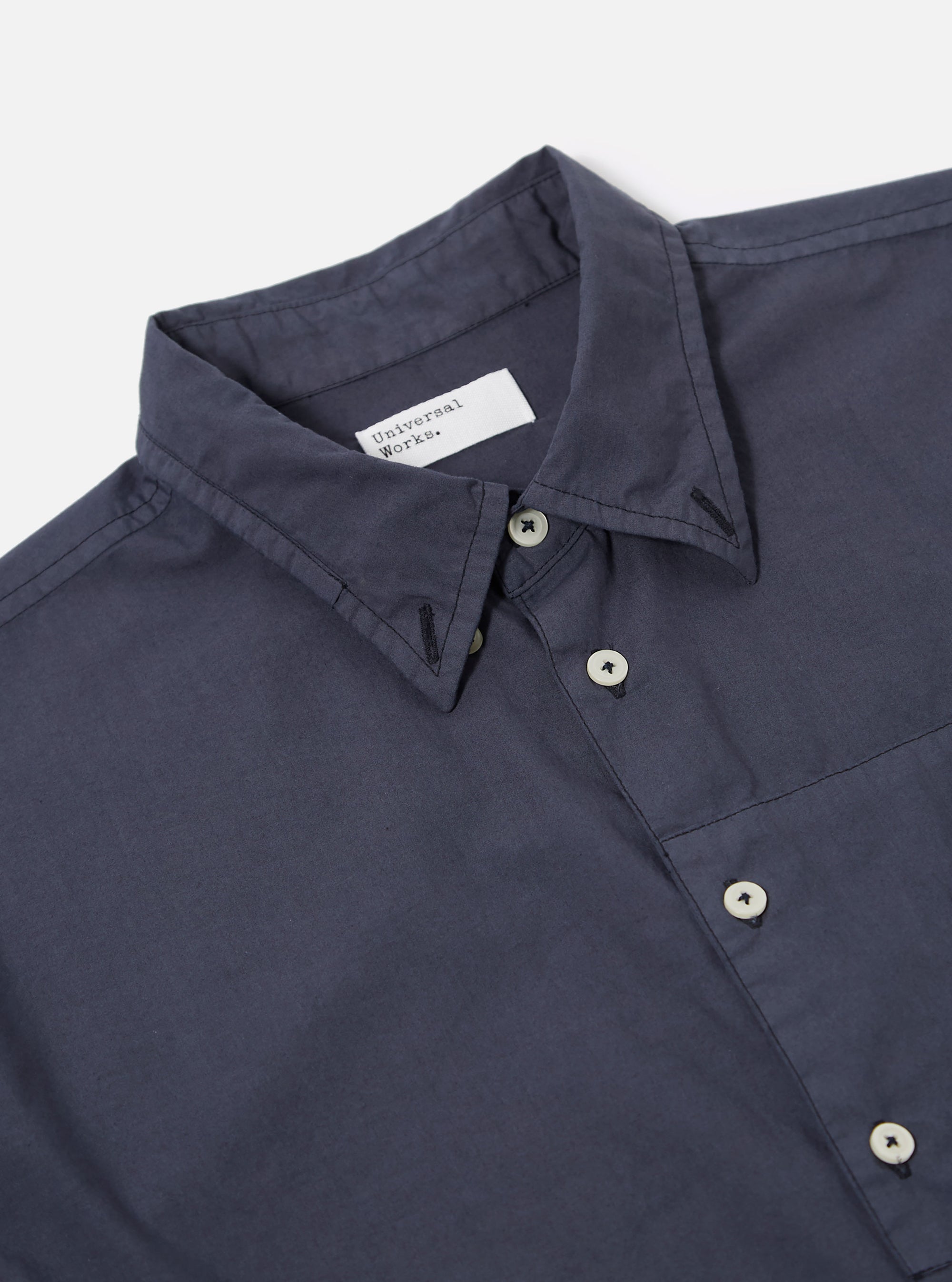 The Navy Poplin Patched Lazy Day Shirt is shown from a rear angle as a flat lay against a plain white background. The image highlights the smooth navy blue poplin fabric, a simple straight hem, and a clean back yoke with a central box pleat.