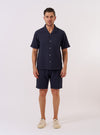 The Navy Dot Waffle Road Shirt is shown as a flat lay against a plain white background. The shirt features a camp collar, a single chest patch pocket, and a central button-down front with mother-of-pearl buttons. The navy blue cotton fabric has a distinct rounded waffle-dot texture throughout.