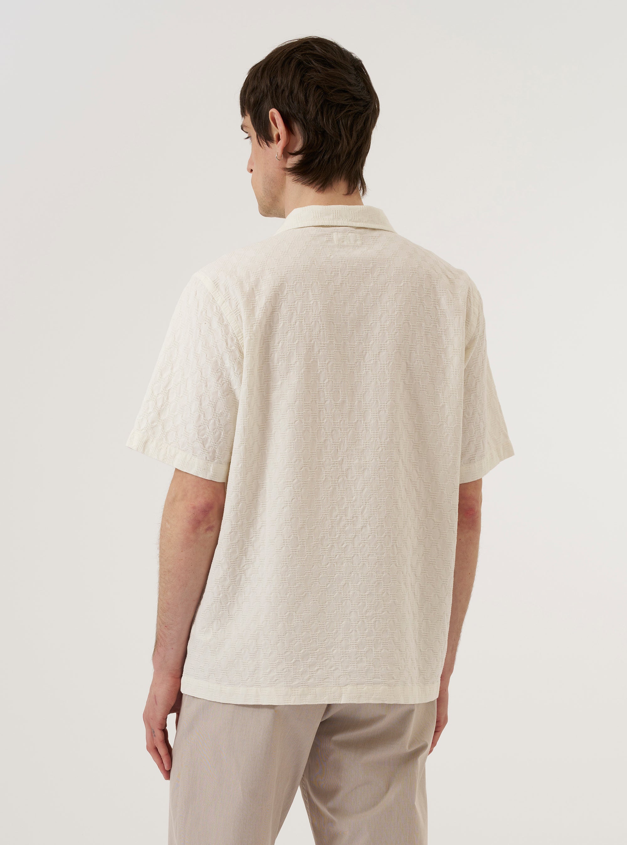 A model wears the Ecru Dot Waffle Road Shirt, featuring a camp collar, short sleeves, and a textured dot waffle fabric. The model is photographed from the waist up against a plain light gray background. The shirt is shown partially unbuttoned over a white t-shirt.