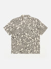 The Ecru/Black Kantha Flower Road Shirt is shown as a flat lay against a white background. The short-sleeve shirt features a camp collar, a central button-down front, and a single patch pocket on the left chest. The ecru fabric is detailed with an all-over black floral embroidery pattern.