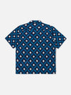 The Indigo Diamond Ikat Deck Shirt is presented from the rear as a flat lay against a white background. The shirt features a horizontal yoke across the shoulders and a straight hem. The fabric is decorated with a repeating white diamond ikat pattern on a dark indigo base.