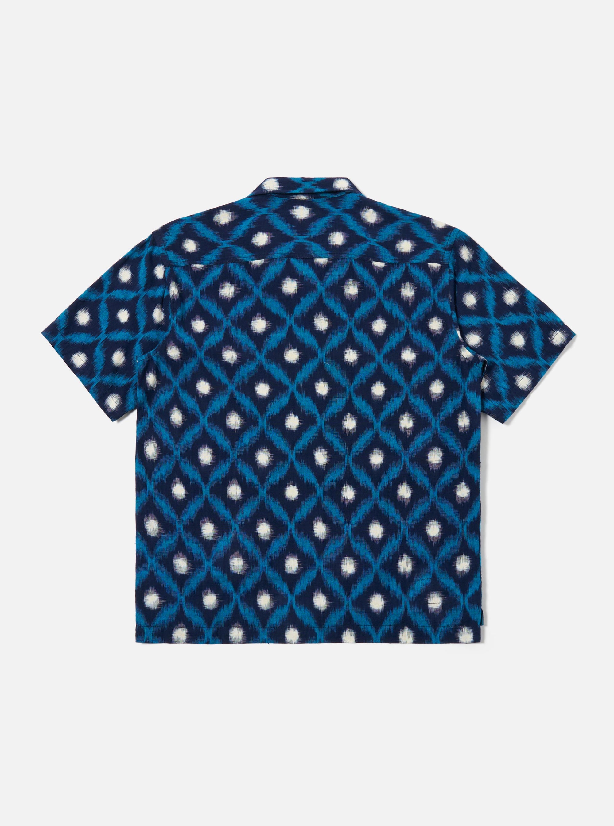 The Indigo Diamond Ikat Deck Shirt is presented from the rear as a flat lay against a white background. The shirt features a horizontal yoke across the shoulders and a straight hem. The fabric is decorated with a repeating white diamond ikat pattern on a dark indigo base.