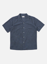 The Indigo Fine Organic Cotton Sal Road Shirt is shown as a flat lay against a plain white background. The shirt features a camp collar, a central button-down front with tonal buttons, and two large chest patch pockets with buttoned flaps. The fabric is a deep indigo blue organic cotton with a smooth, lightweight appearance.