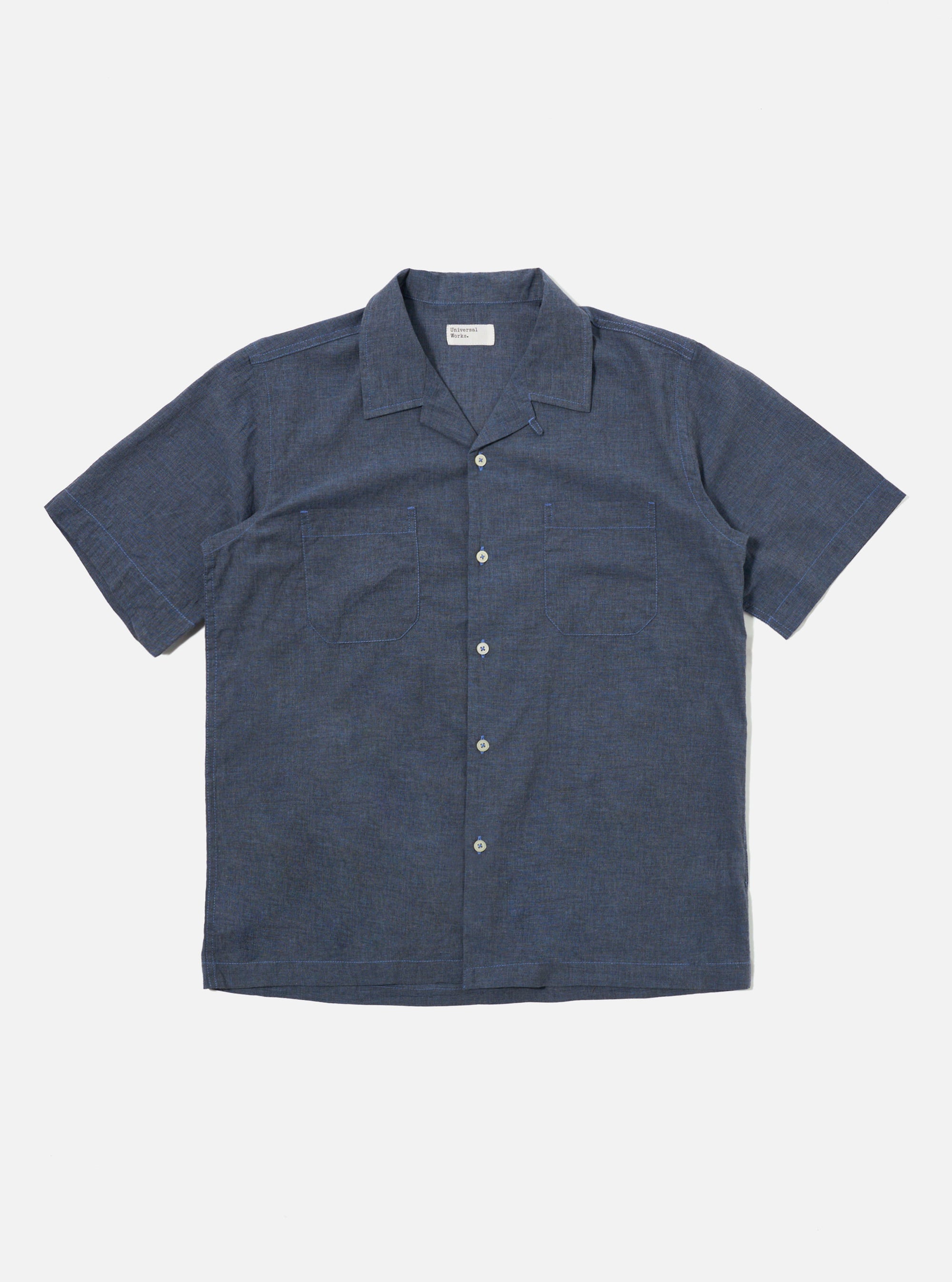 The Indigo Fine Organic Cotton Sal Road Shirt is shown as a flat lay against a plain white background. The shirt features a camp collar, a central button-down front with tonal buttons, and two large chest patch pockets with buttoned flaps. The fabric is a deep indigo blue organic cotton with a smooth, lightweight appearance.
